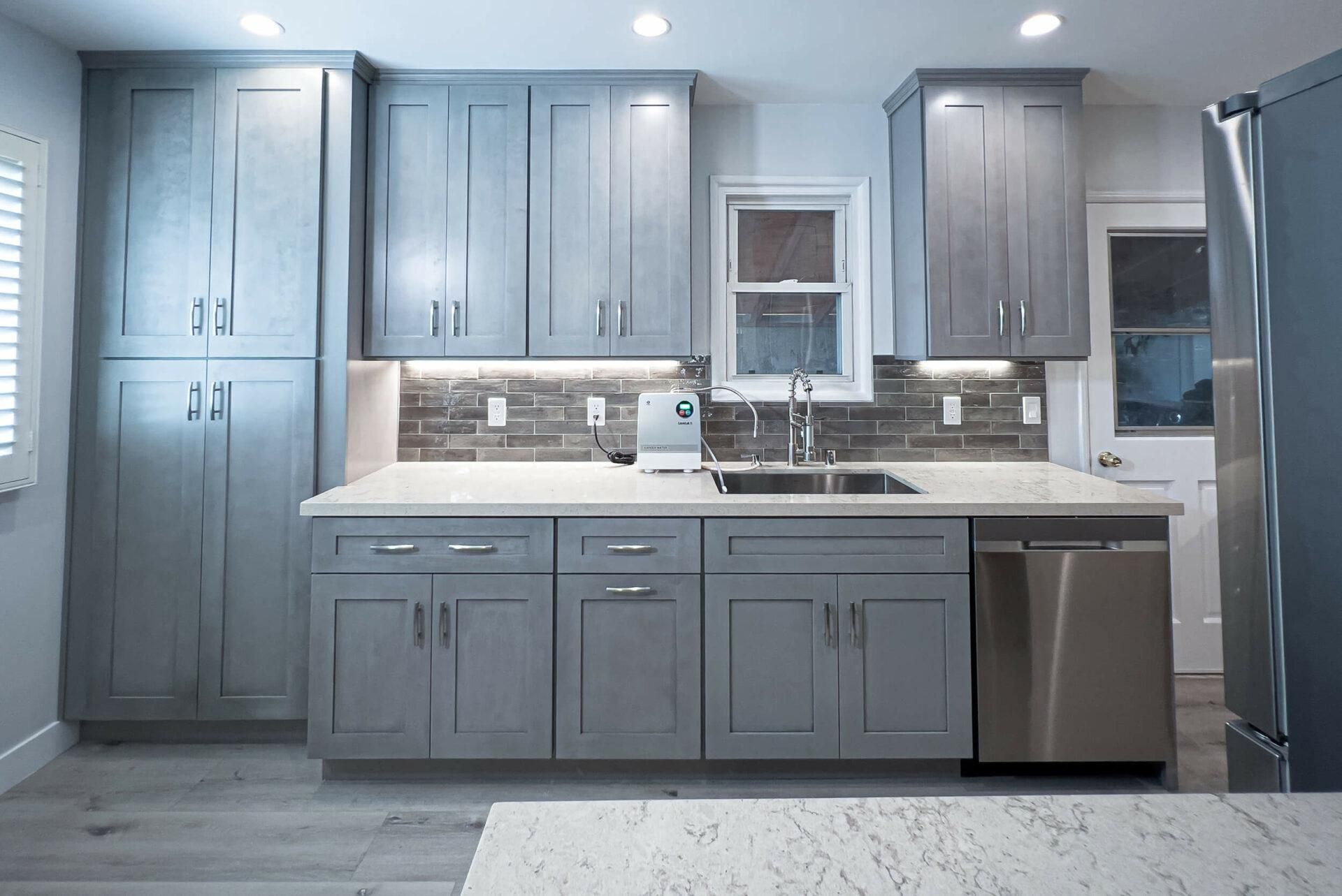 A kitchen with gray cabinets , stainless steel appliances , a sink and a refrigerator.