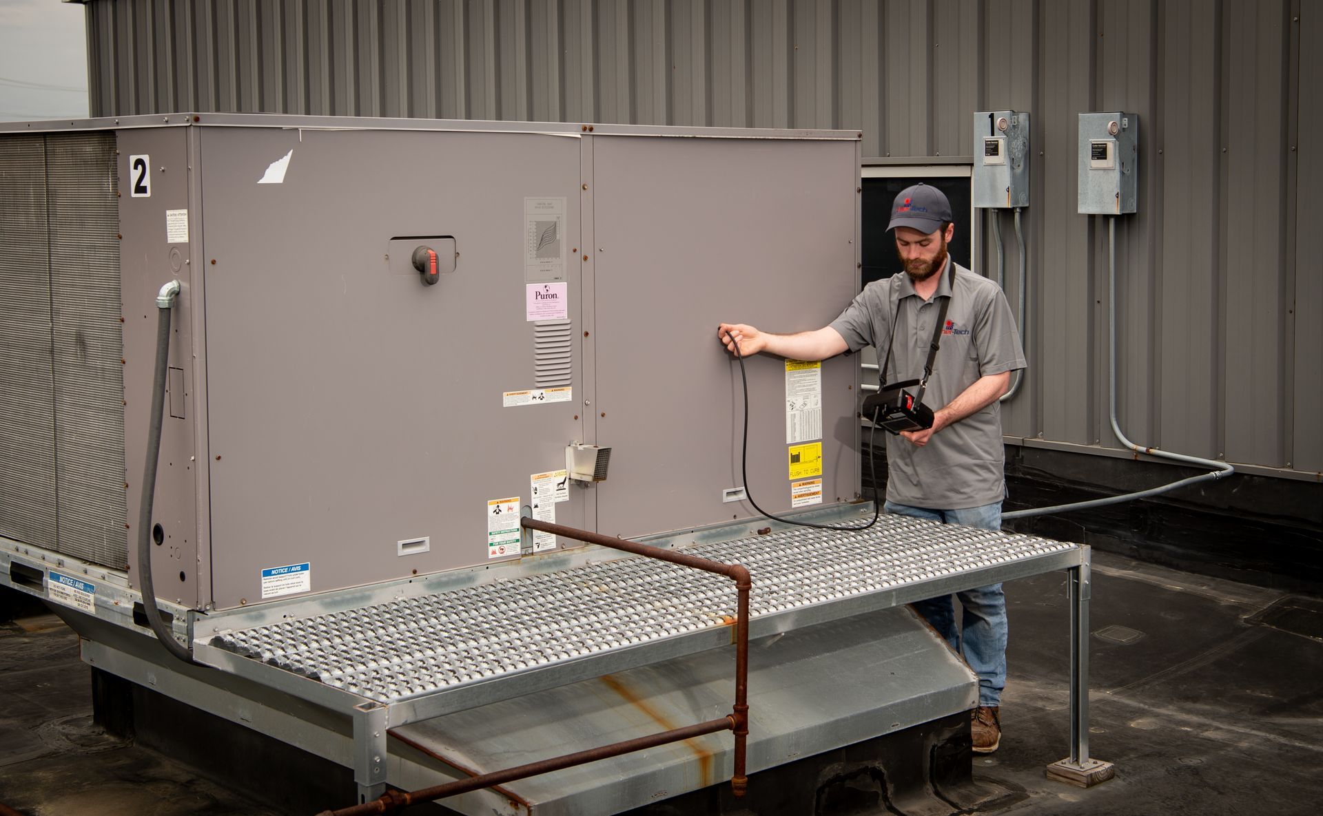 A man is standing next to a large air conditioner on the roof of a building.