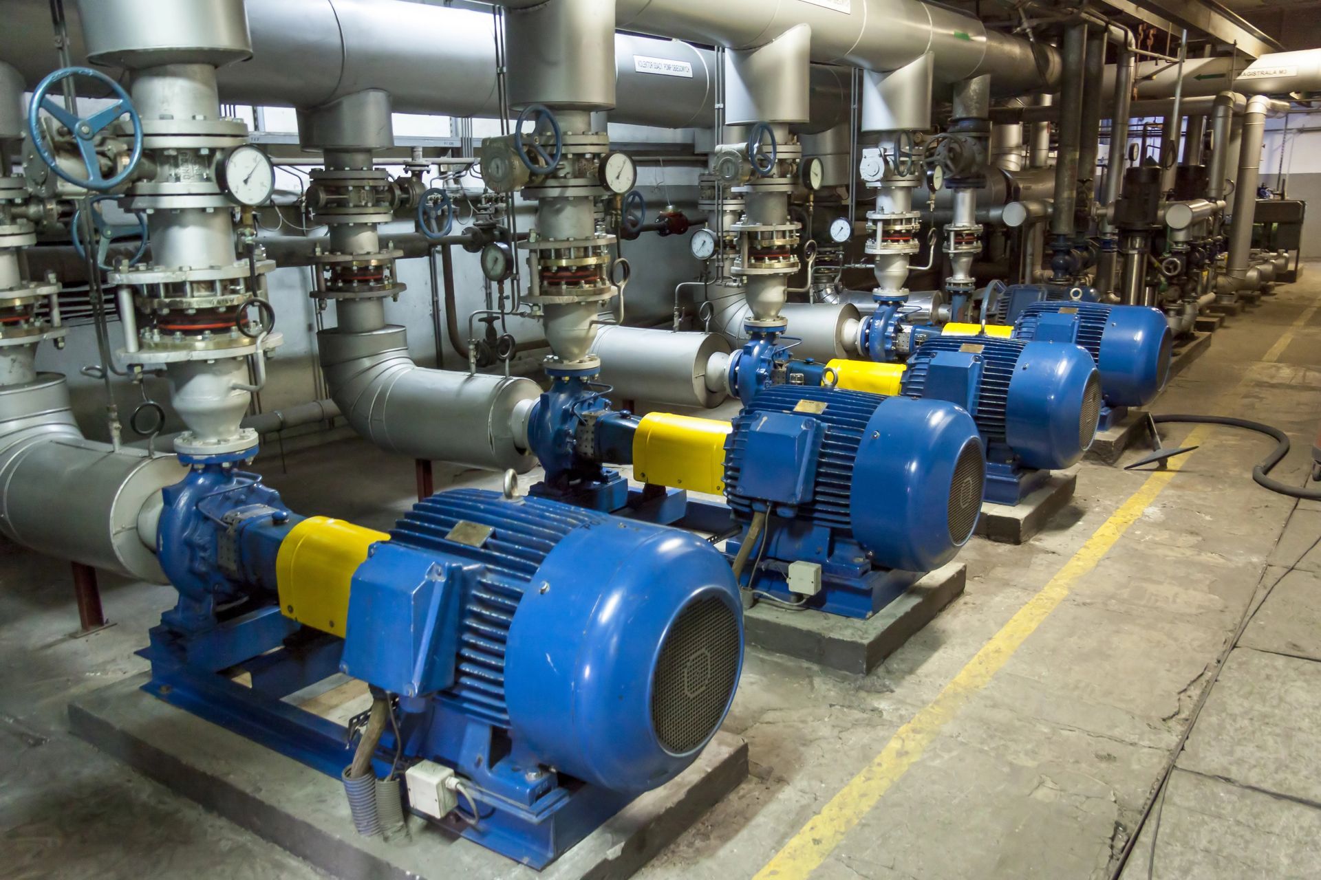 A row of blue pumps and pipes in a factory.