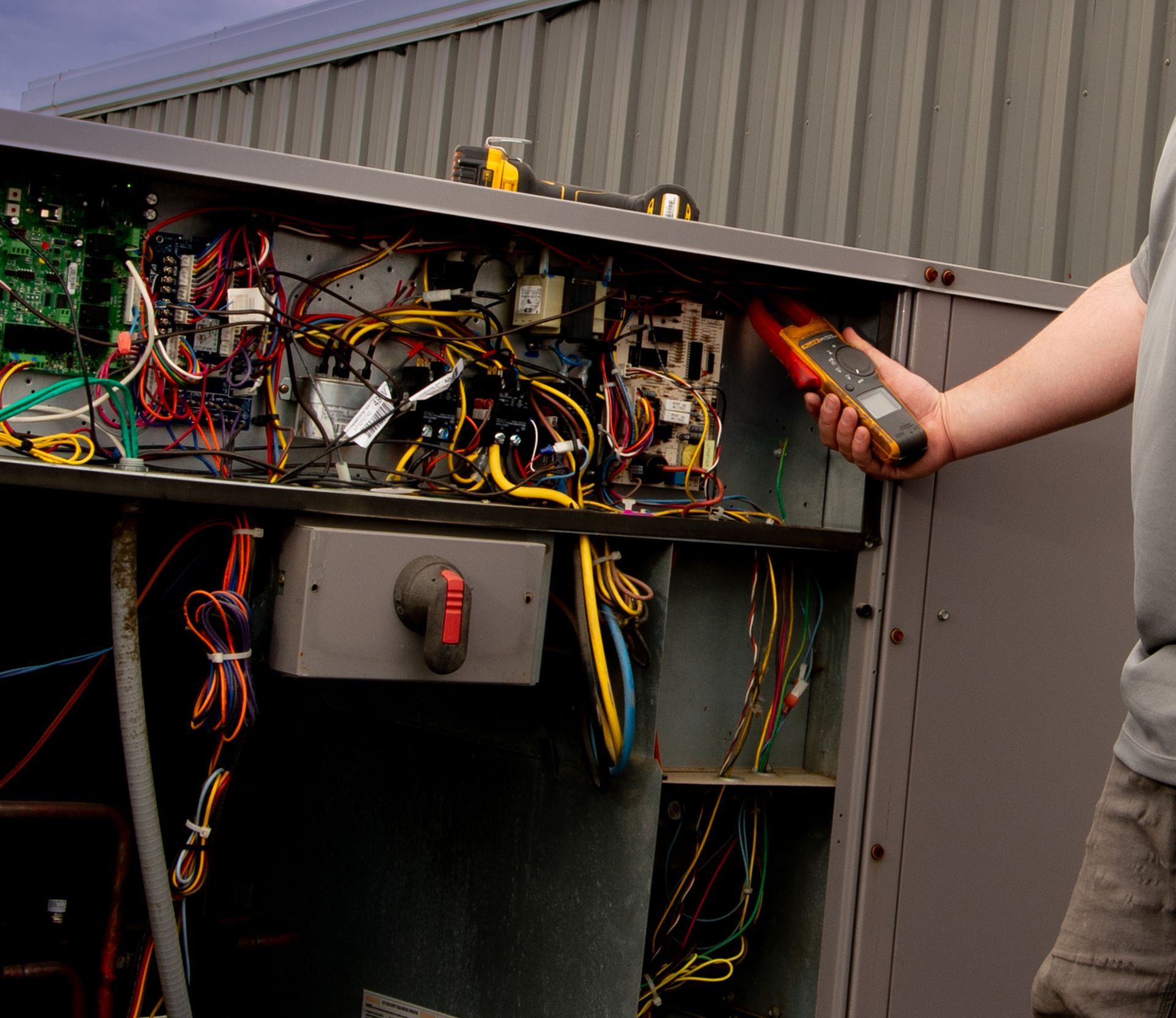 A man is holding a multimeter in front of an electrical box.