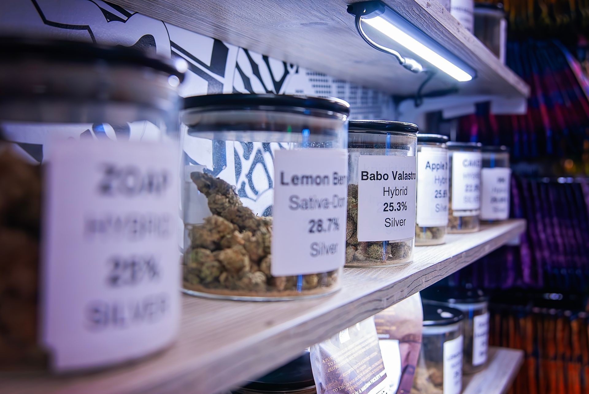 Shelves with jars of cannabis strains labeled with names and percentages.