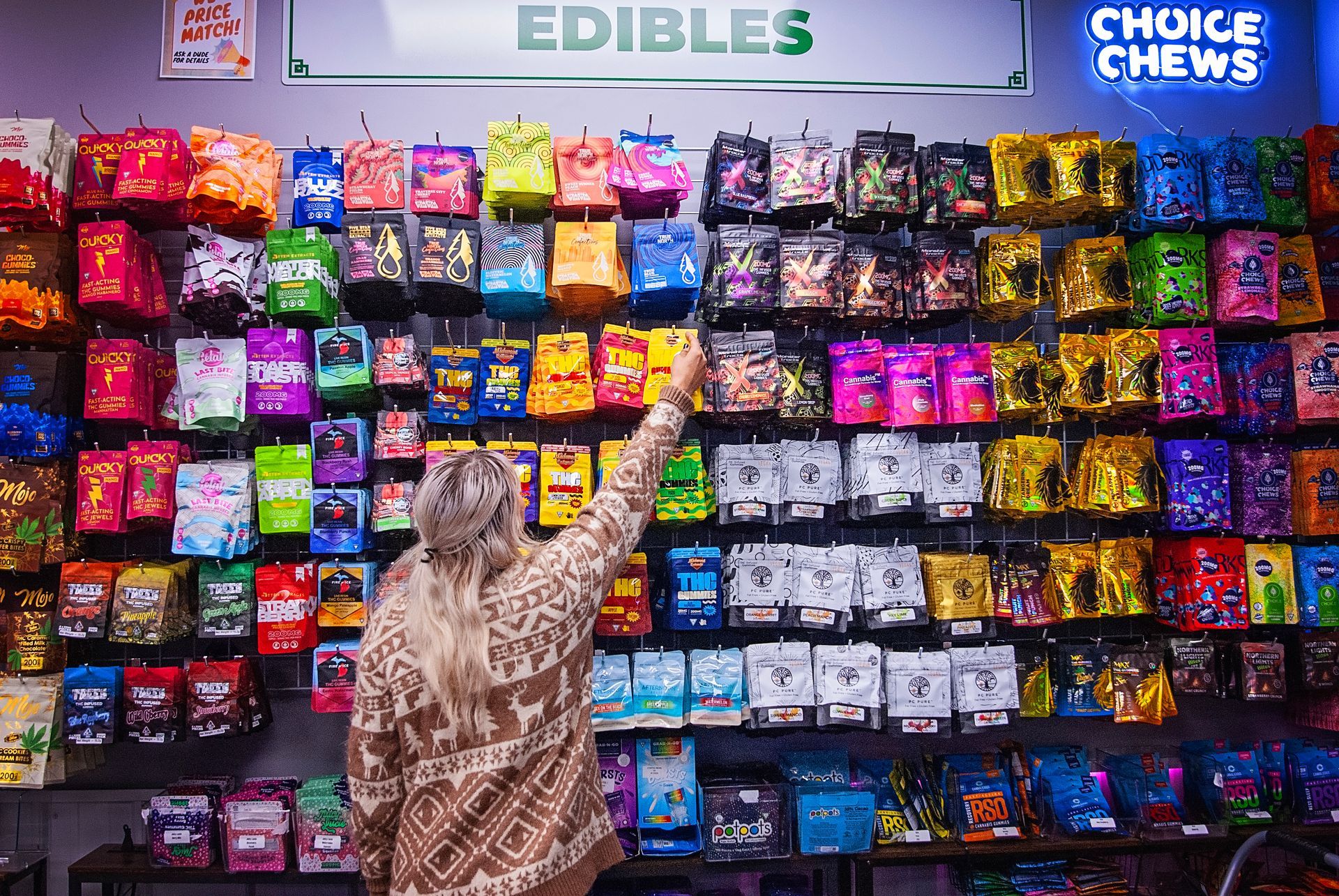 A woman is standing in front of a wall of candy in a store.
