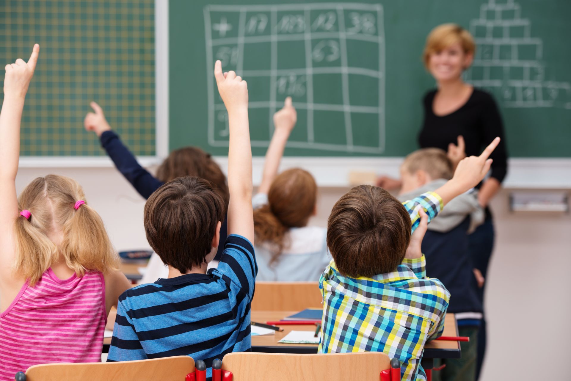 a group of children are raising their hands in a classroom to answer a question