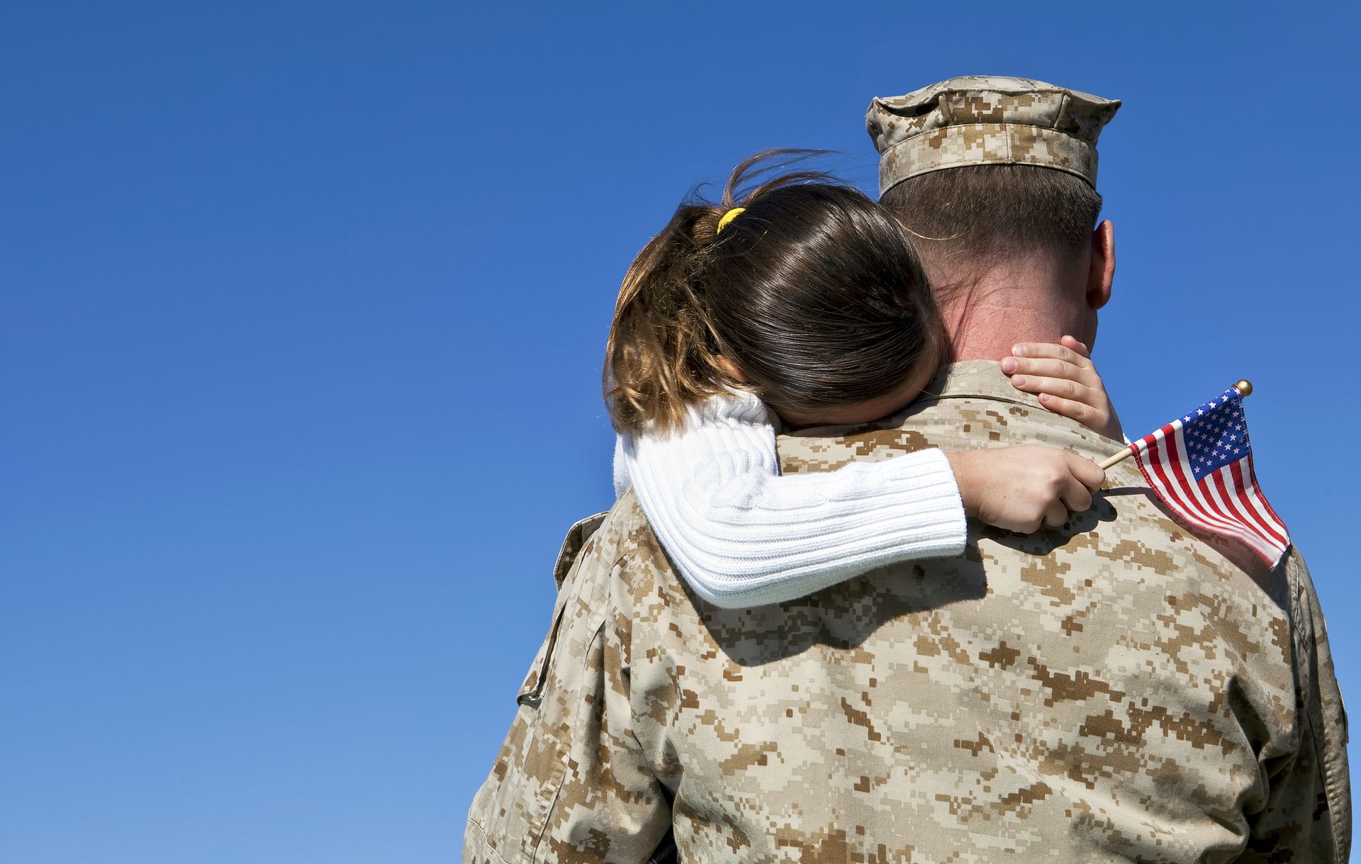 a soldier is hugging a little girl who is holding an american flag