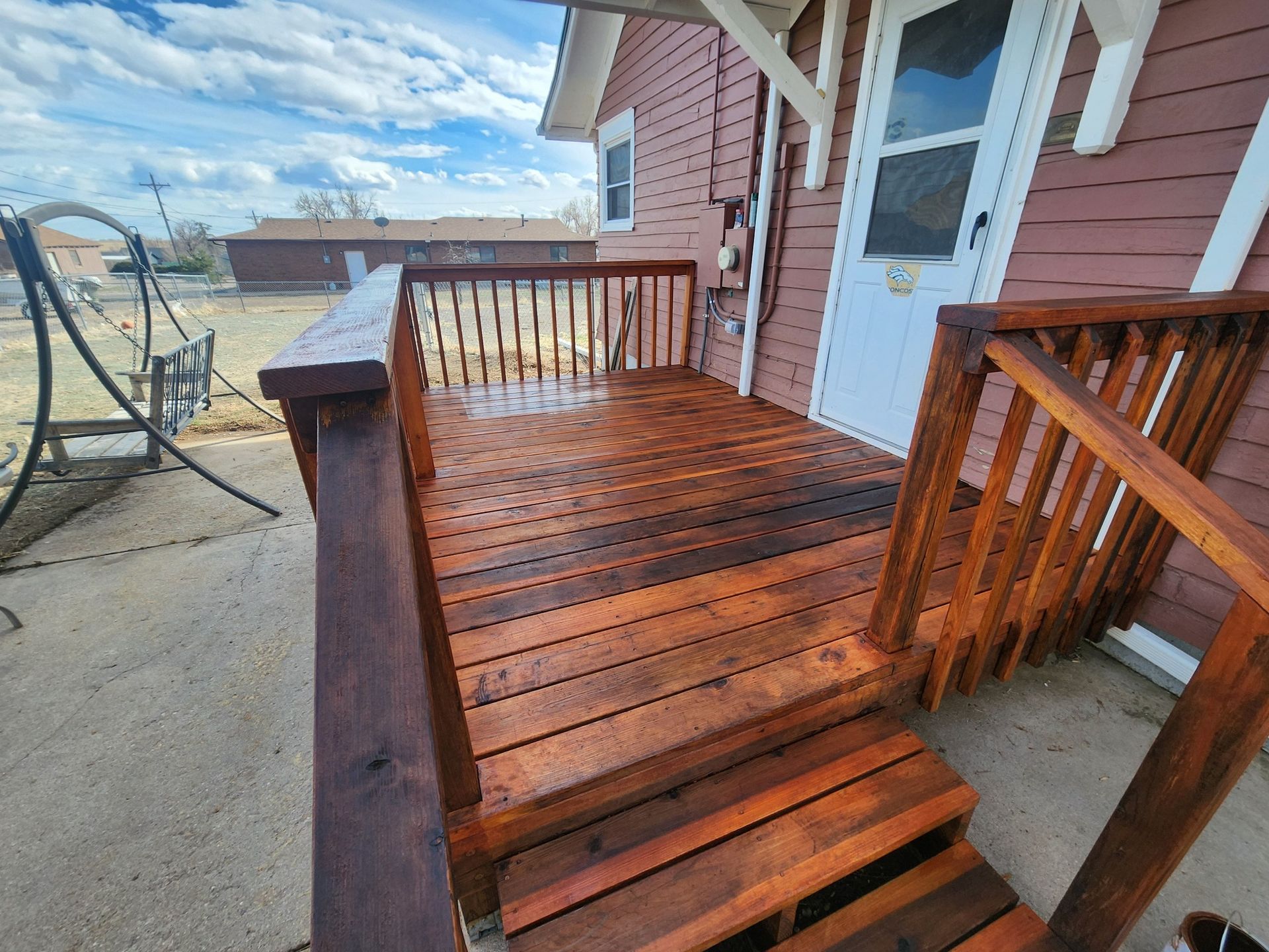 A wooden deck with stairs leading to the front door of a house.