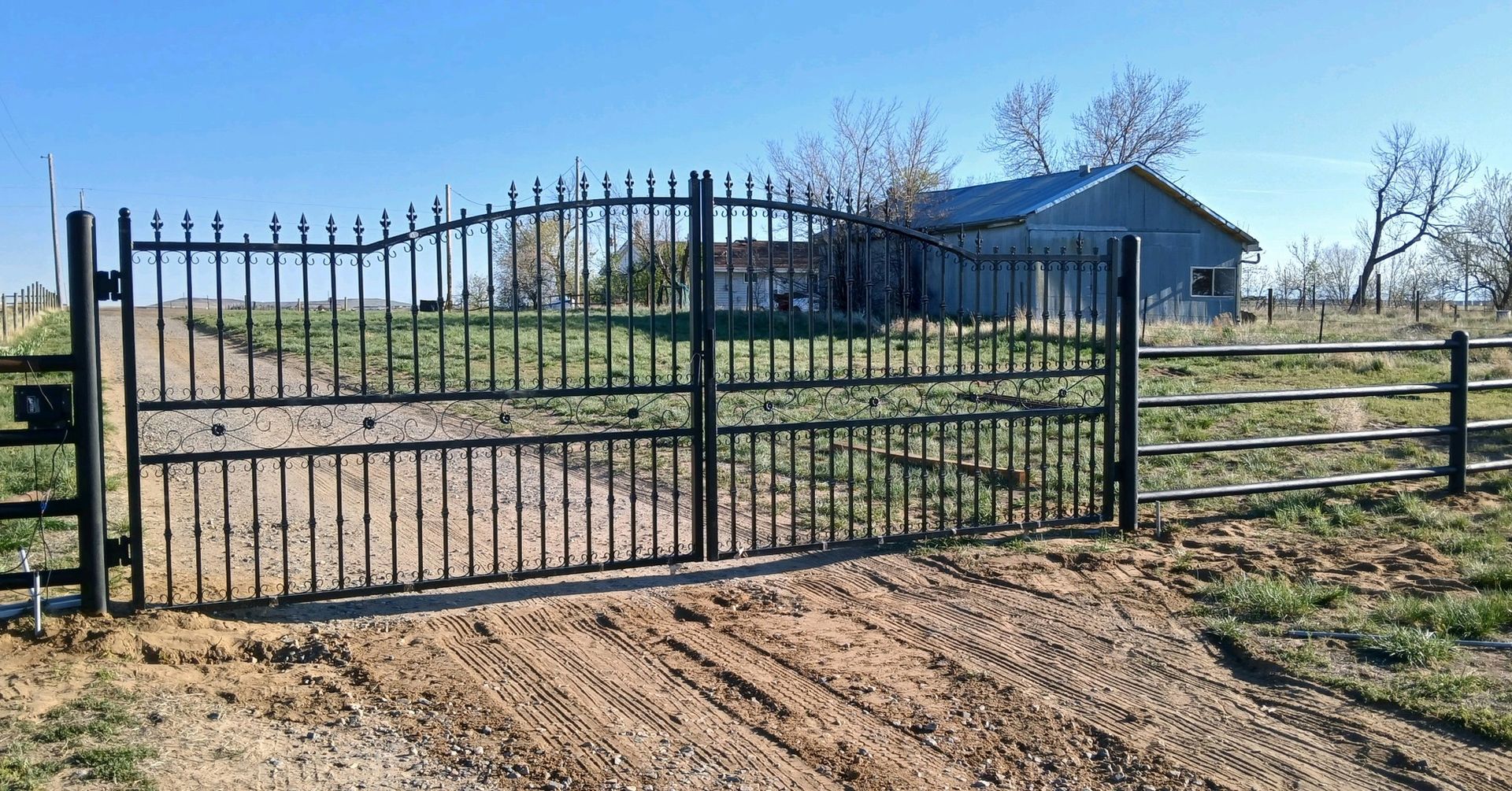 A metal gate is sitting on the side of a dirt road in front of a house.