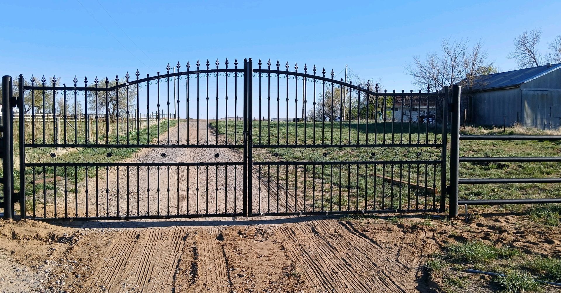 A wrought iron gate is sitting in the middle of a dirt field.
