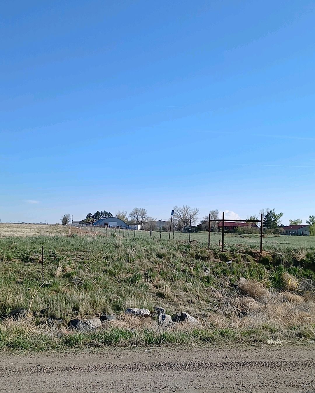 A dirt road going through a grassy field with a house in the background.