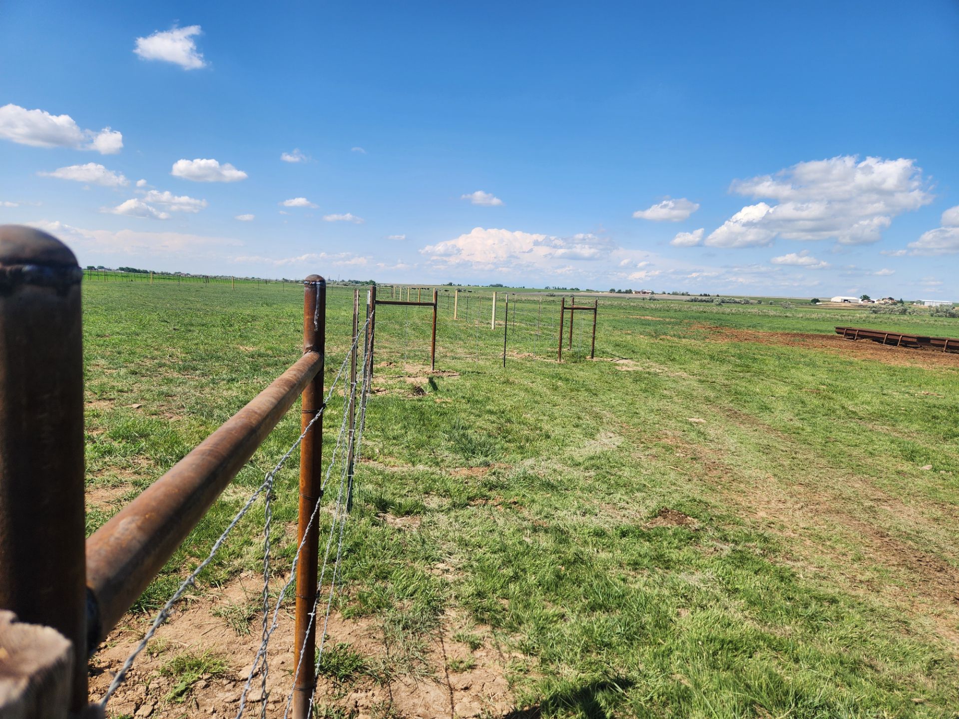 A wooden fence surrounds a grassy field on a sunny day.