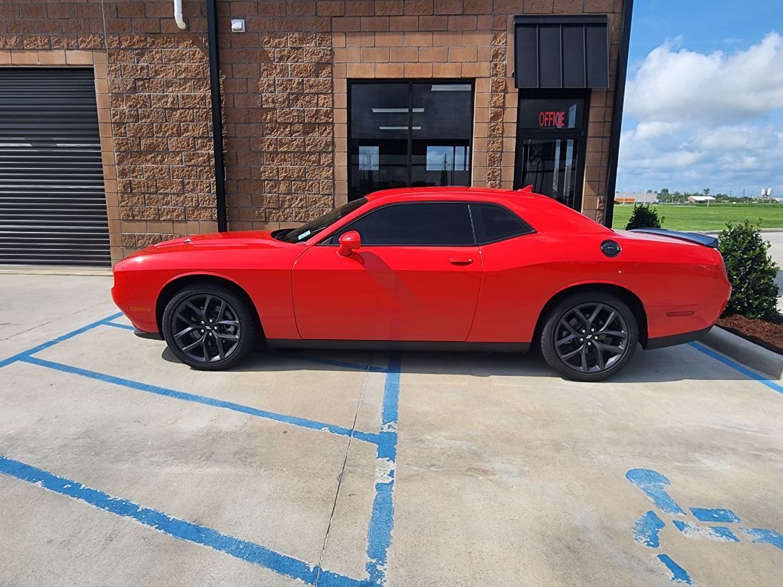 A red dodge challenger is parked in a handicapped parking spot in front of a building.