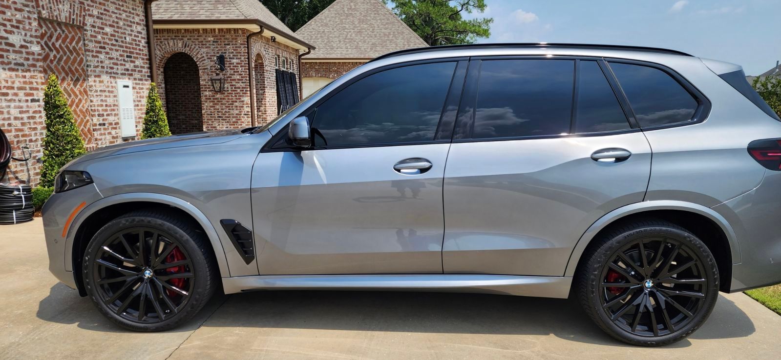 A silver bmw x5 m sport is parked in a driveway in front of a brick house.