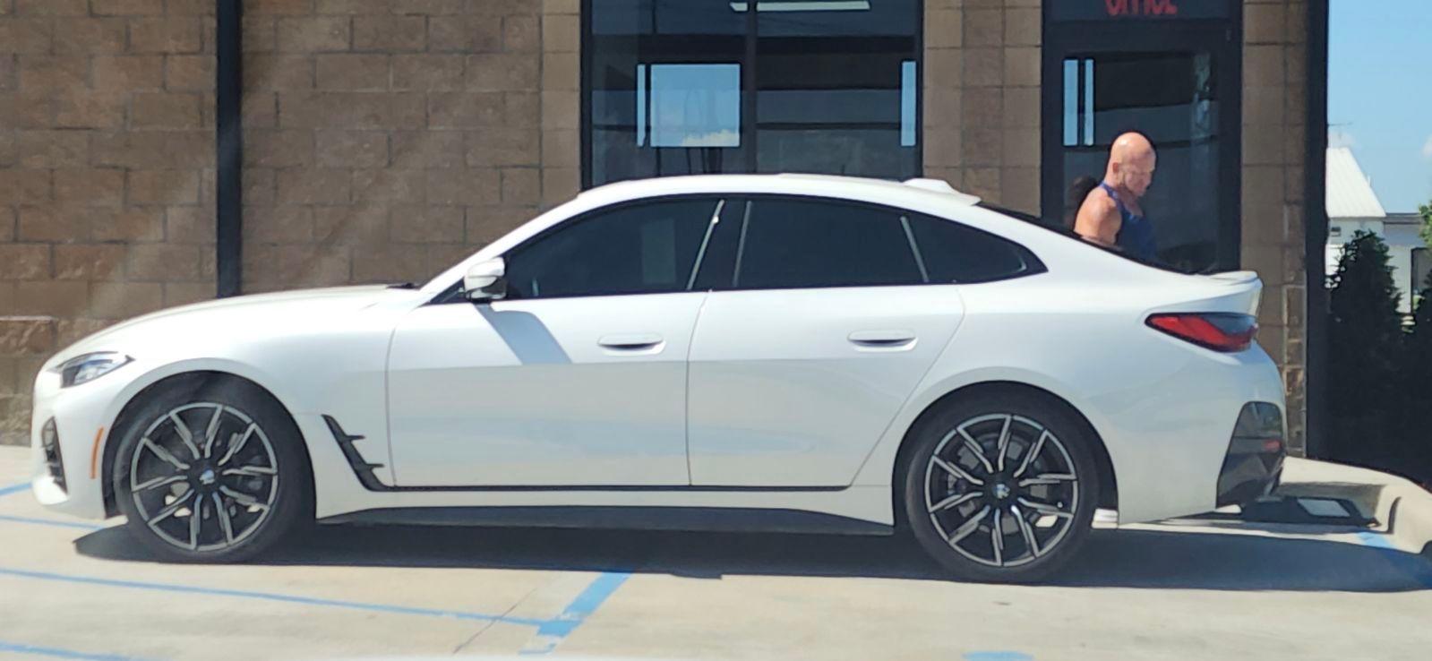 A white car is parked in a parking lot in front of a building.