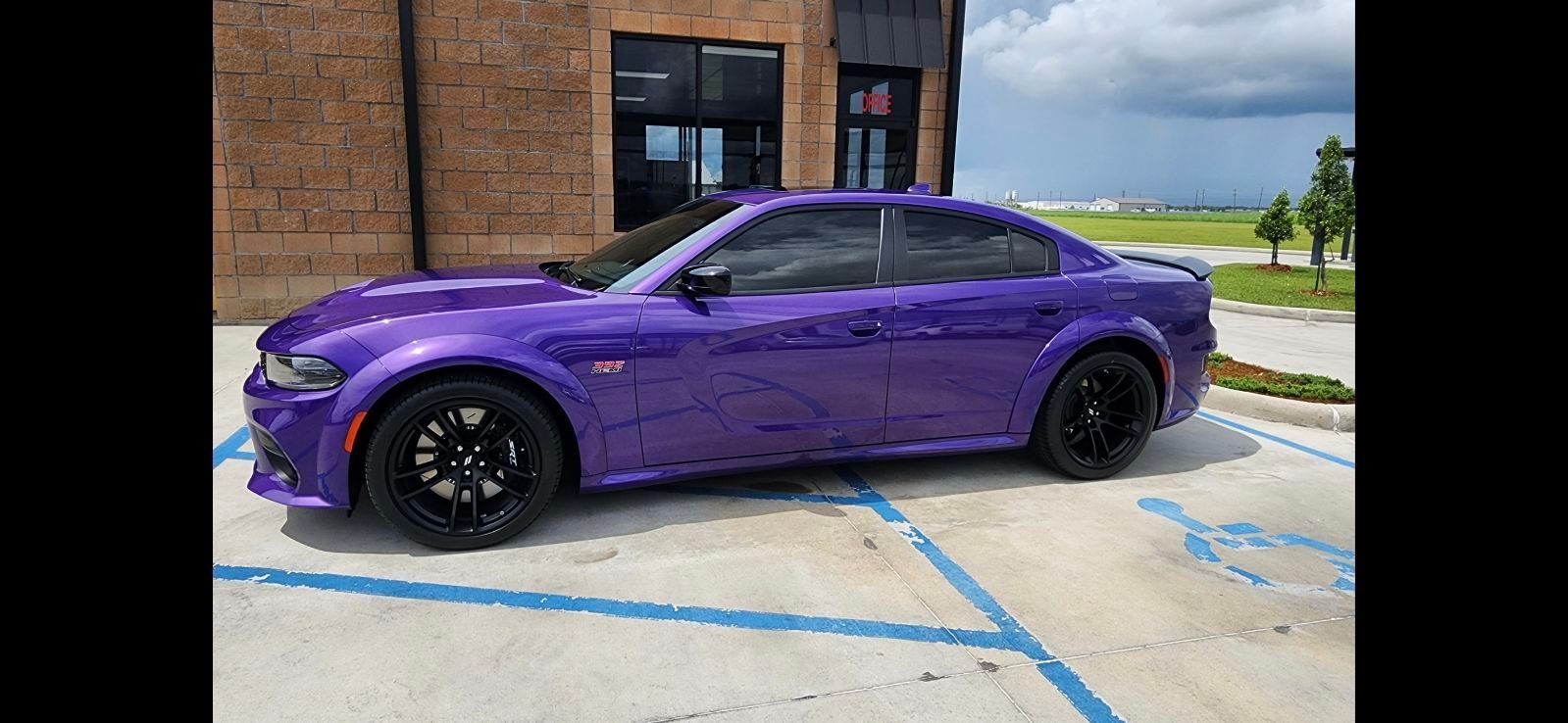 A purple dodge charger is parked in a parking lot in front of a building.