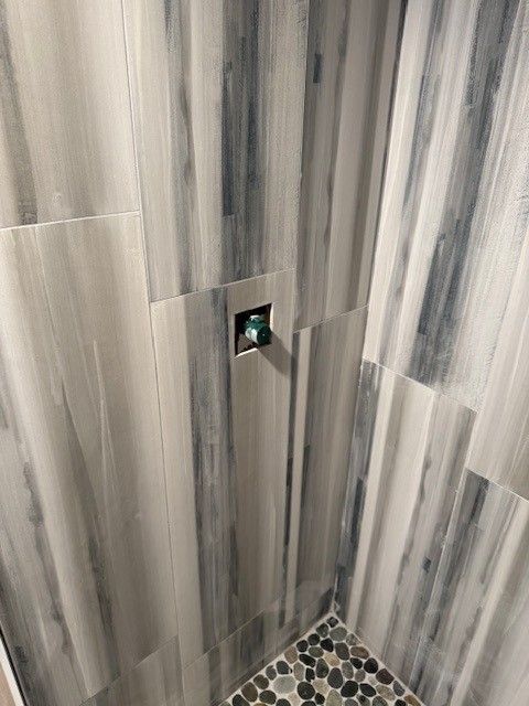 Shower with gray and white wood-look tile walls, pebble floor, and a silver faucet installed by Steen & Son Plumbing and Heating