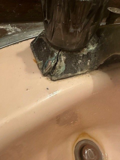 Close-up picture of a corroded faucet base on a pink sink before remodel done by steen & son plumbing and heating
