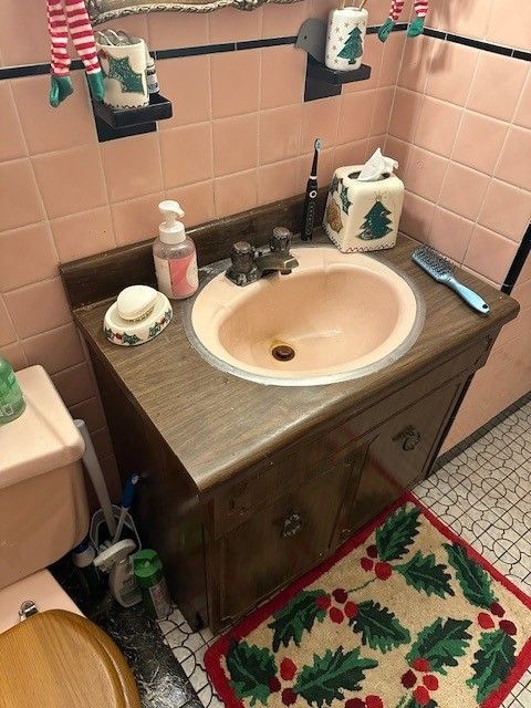 Pink-tiled bathroom with a brown vanity and a pink sink before remodel done by steen & son plumbing and heating