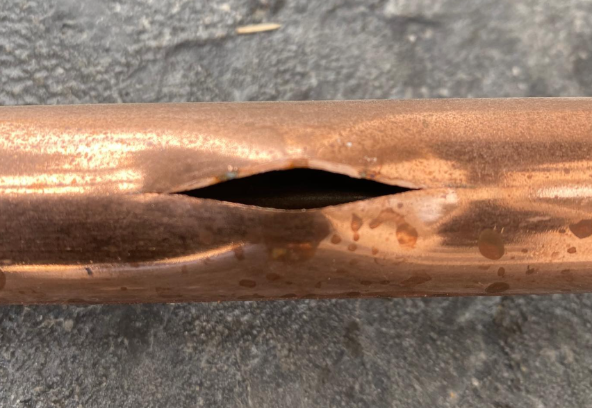 A copper pipe with a large, elongated split in its side being fixed by Steen & Son Plumbing and Heating in Mays Landing, New Jersey