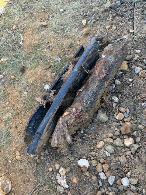 Two broken, dark-colored wooden beams holding a broken sewage pipe between them