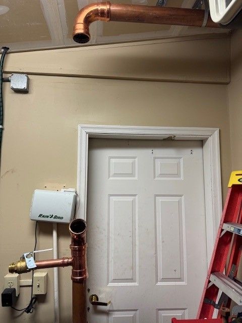 a copper, commercial 3 inch line against a beige wall, above a white door with a ladder is on the right