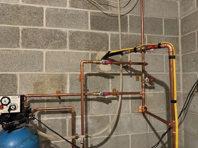 Copper pipes and valves against a gray cinder block wall, part of a plumbing system repair done by steen & son plumbing and heating