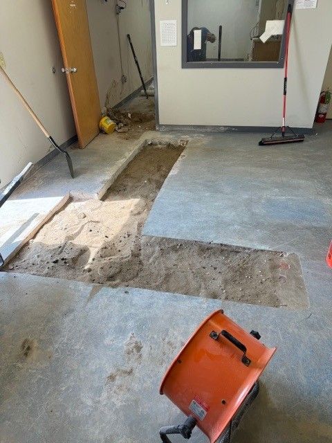 Concrete floor with a trench dug out; an orange fan is in the foreground
