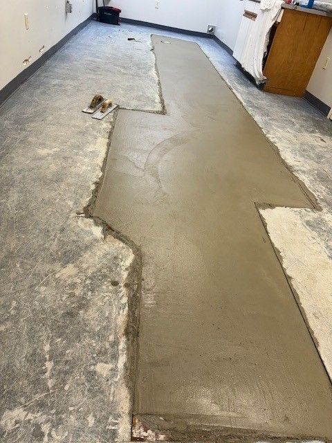 Newly poured concrete section on a gray floor in a room, ready for leveling by steen & son plumbing and heating