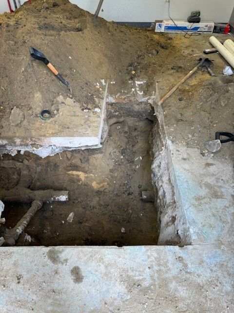 A hole dug in concrete floor with exposed pipes in atlantic county, new jersey by steen & son plumbing and heating