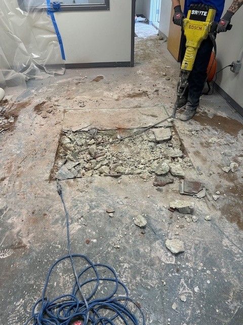 A steen & son plumbing technician using a jackhammer to break up concrete flooring to repair a plumbing pipe