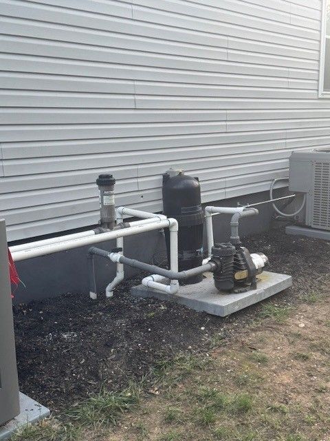 Pool equipment on the side of a house that includes a pump, filter, and plumbing on a concrete pad installed by steen & son plumbing and heating in mays landing, new jersey