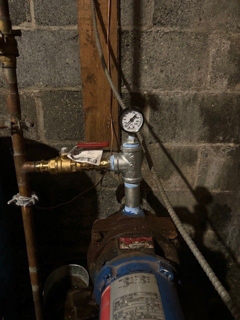 Well water pump with a pressure gauge and a red-handled valve, indoors against a concrete block wall repaired by steen & son plumbing and heating