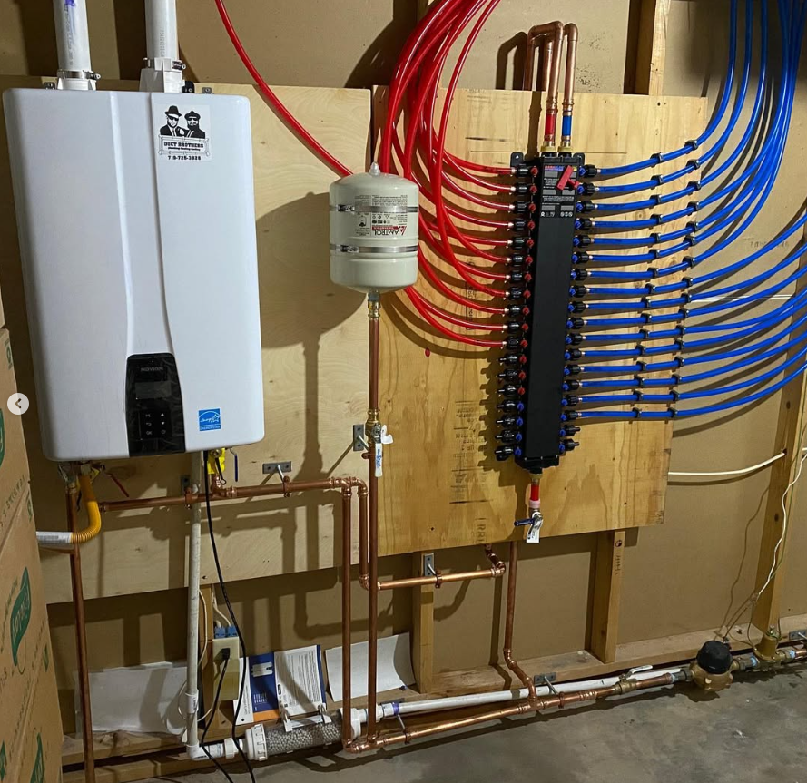 A wall-mounted water heater and hydronic heating system with red and blue PEX tubing installed by Steen & Son Plumbing and Heating in Mays Landing, New Jersey. Copper pipes and a distribution manifold are also visible