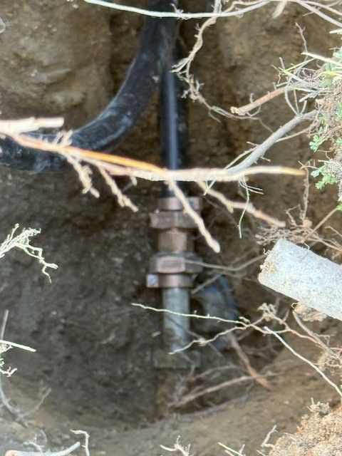 A buried water line connection with metal fittings and black and gray pipes in a dirt trench in atlantic county, new jersey