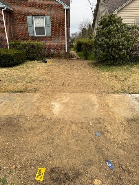 A sandy, cleared path leading to a brick house, flanked by grass and bushes after new water line installation by steen & son plumbing and heating in mays landing, new jersey