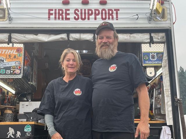 a man and a woman are standing in front of a fire support truck .