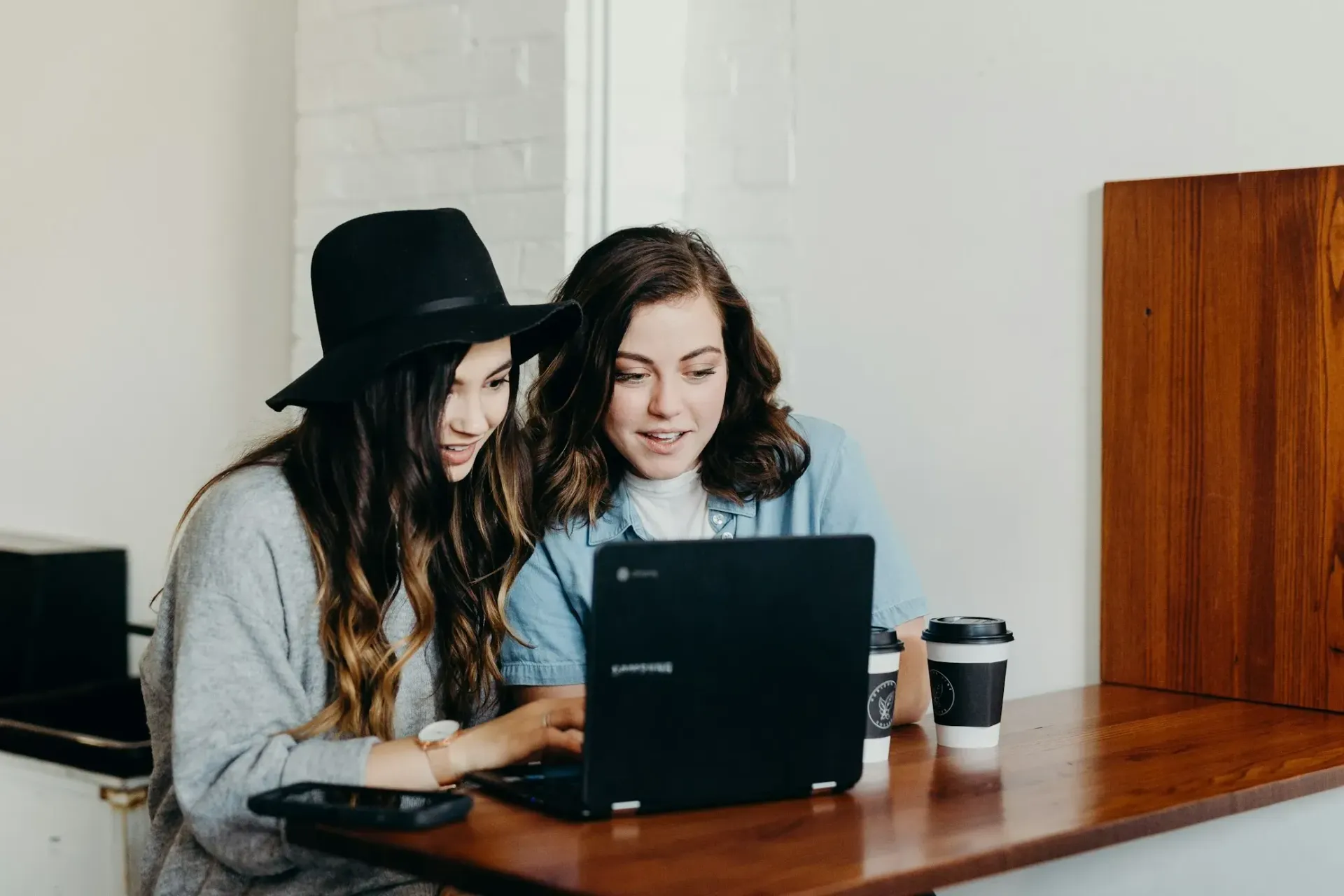 Two women are sitting at a table looking at a laptop computer.