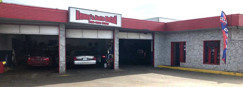 Exterior view of an auto repair shop with red trim, and three garage bays. Cars are parked inside.