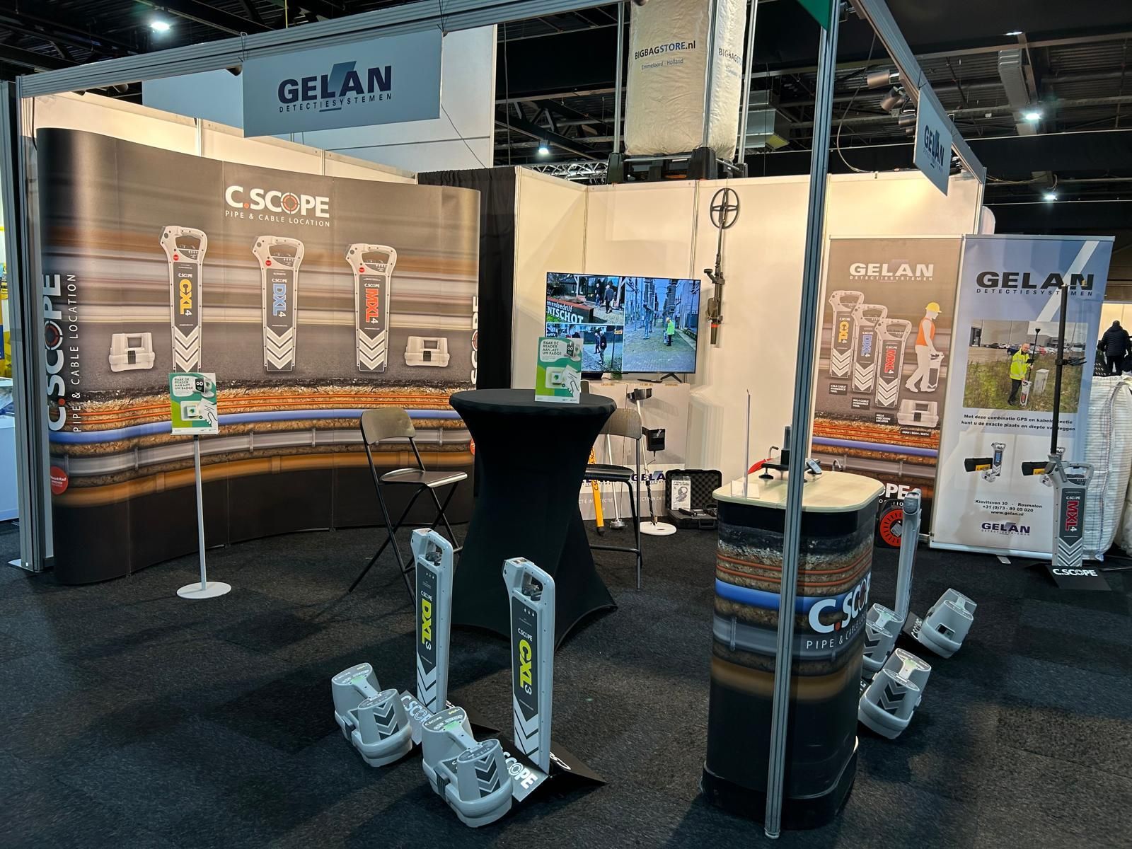 Trade show booth for GFLAN and C.SCOPE featuring promotional displays, equipment on stands, and a black pedestal table.