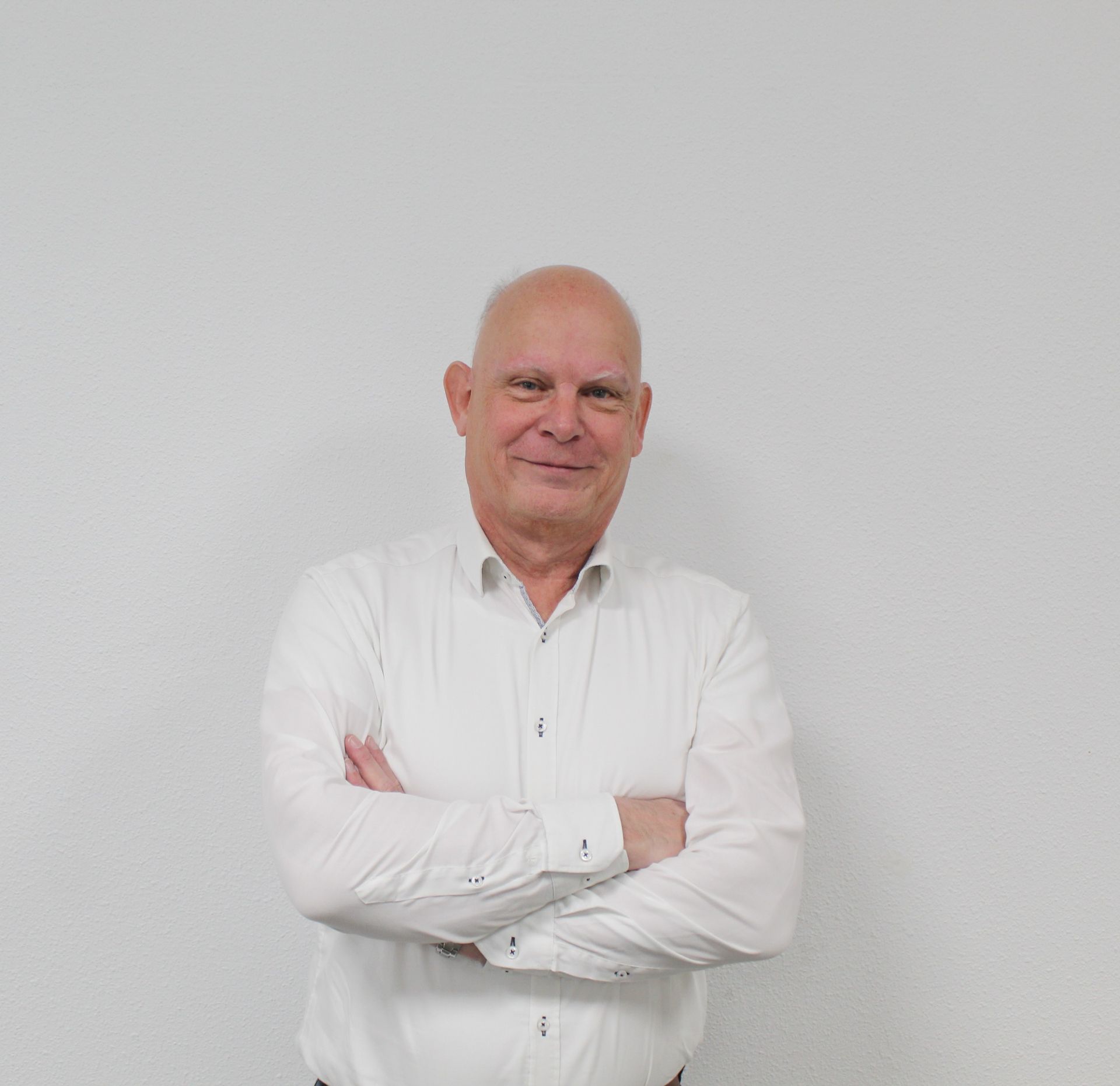 Een kale man in een wit overhemd staat met zijn armen over elkaar.