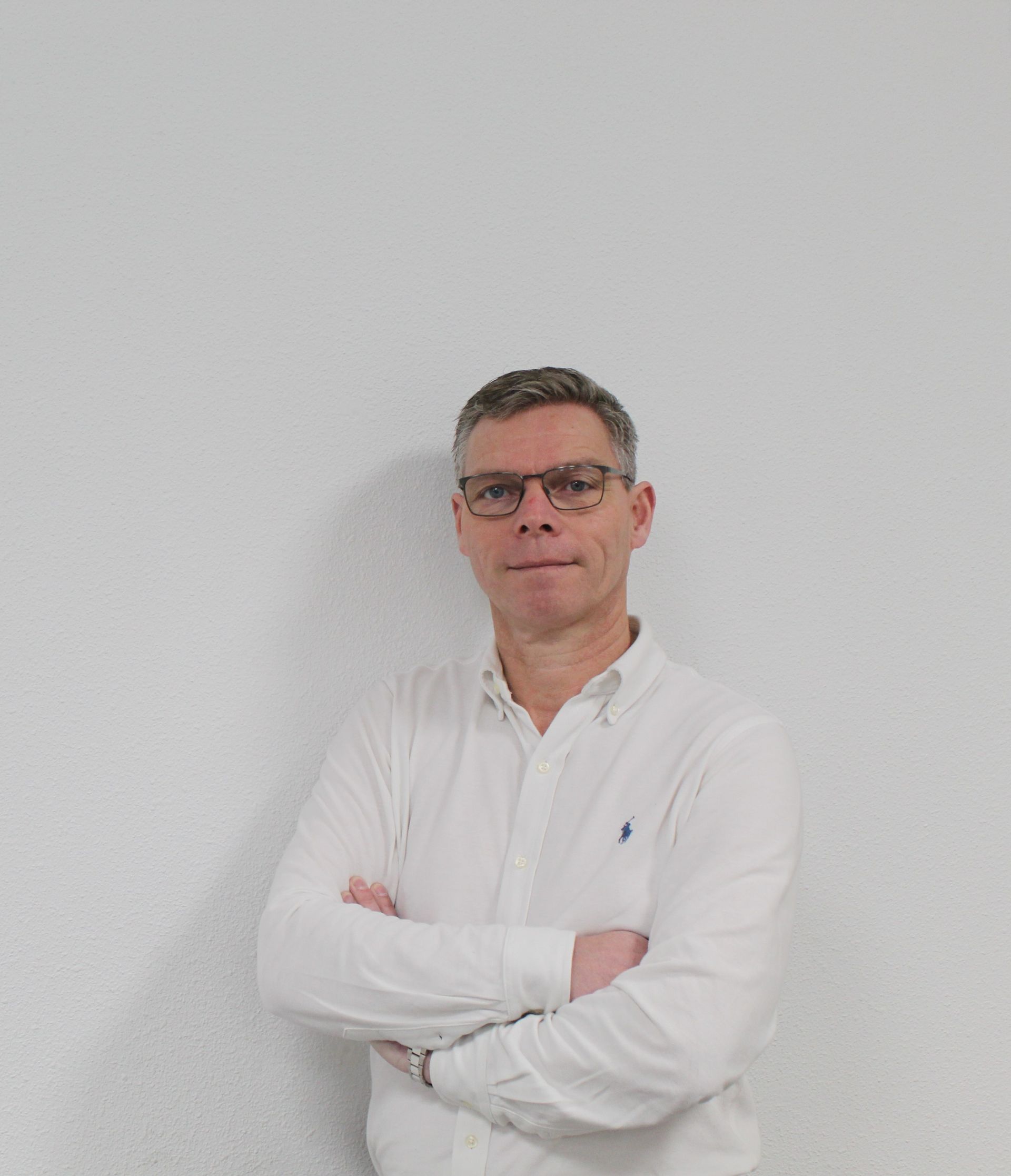 Een man met een bril en een wit overhemd staat met zijn armen over elkaar.