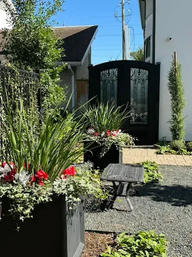 Black entry gate and planters in an outdoor garden with a small table and gravel pathway.