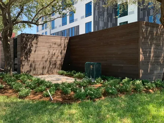 Wooden architectural feature, landscaping with shrubs and grass in front of building.