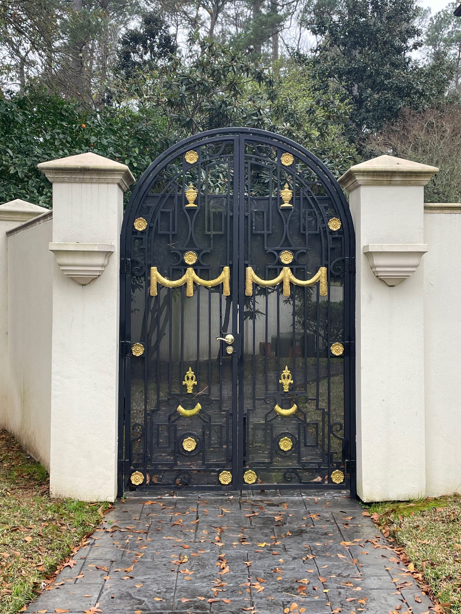 Black ornate wrought iron gate with gold accents, set between white pillars.