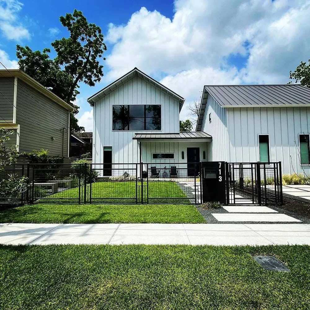 White modern house with black accents, black fence, and green lawn on a sunny day.