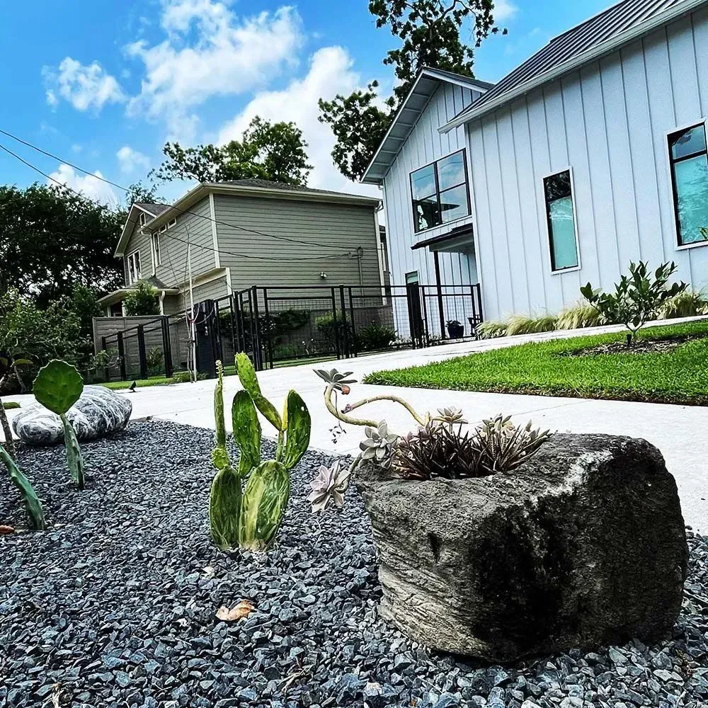 A modern white house with a landscaped yard and a stone planter with succulents.