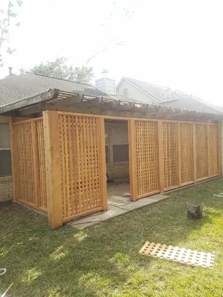 Wooden lattice screen partially enclosing a patio area next to a house with a pergola roof.