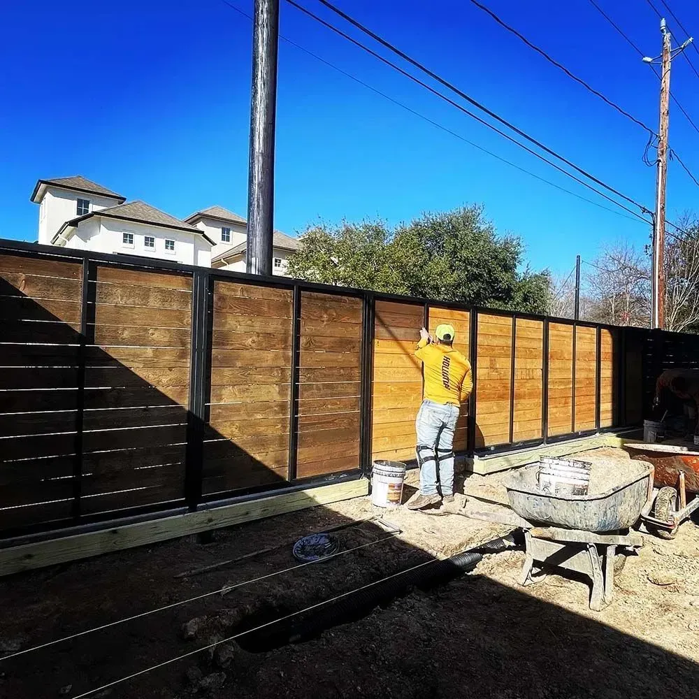 Person painting a wooden fence with black metal frame outdoors on a sunny day.