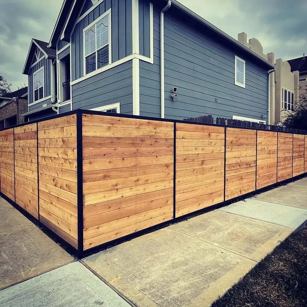 Wooden fence with black frame surrounding a blue house and sidewalk.