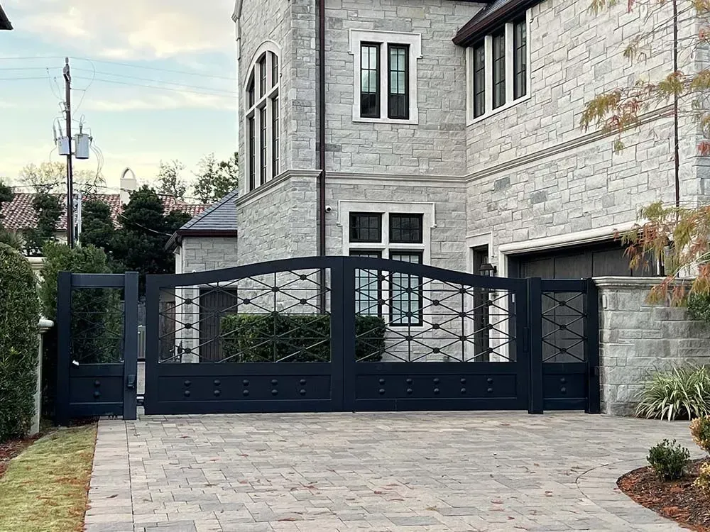 Black wrought iron gate in front of a stone mansion with a brick driveway.