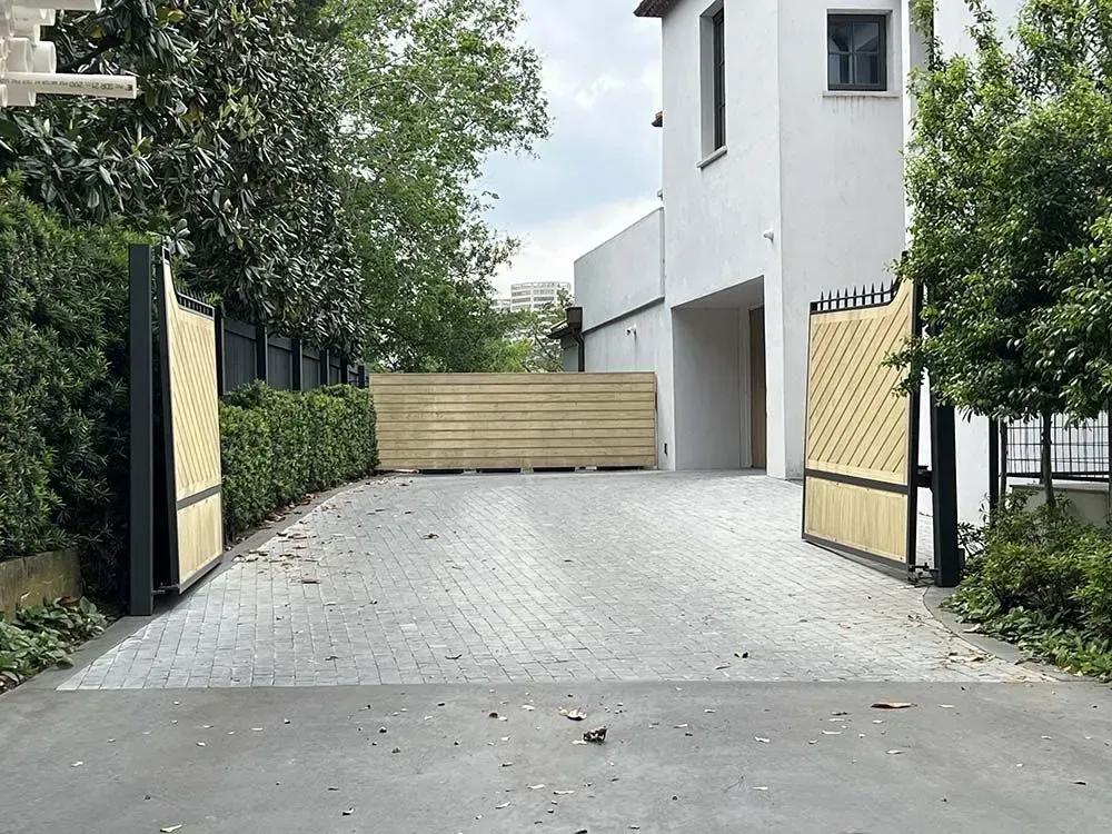 Open, light-colored gates lead to a driveway and modern white house, surrounded by greenery.