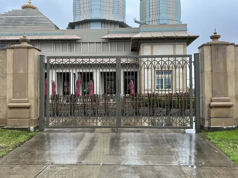 Exterior view of a building behind an iron gate; wet concrete. Beige and gray colors, overcast sky.